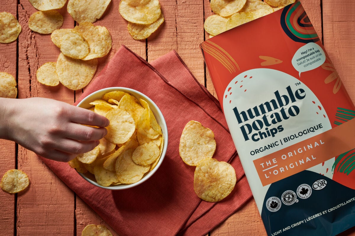 Bowl of Humble Potato chips on wood table top beside a bag of original Humble potato chips